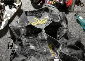Detail of distressed grey denim vest featuring vintage embroidery and ripped texture