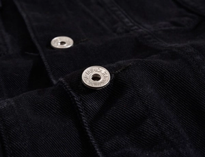Detail of silver metal button with engraved lettering on black denim jacket texture