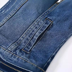 Gros plan d'une poche de veste en jean bleu foncé avec coutures jaunes et texture délavée