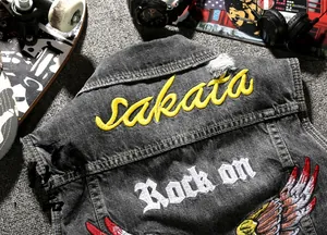 Detail of grey denim vest featuring yellow sakata and white Rock on embroidery and eagle wings