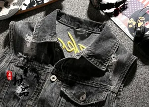 Detail of yellow embroidery on grey distressed denim vest with metallic buttons