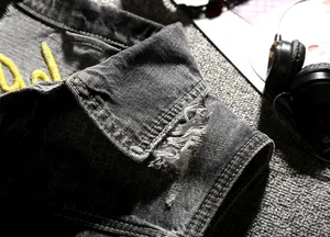Detail of grey distressed denim vest showing torn hole craft and yellow embroidery