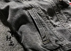 Detail of grey denim vest featuring classic yellow stitching and distressed ripped edges