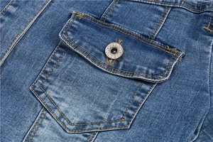 Detail of blue denim cropped jacket showing flap pocket with vintage metal button and stitching