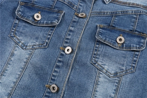 Detail of blue denim jacket showing flap pockets and silver buttons with yellow stitching