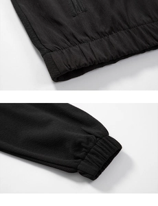 Close-up of black tracksuit jacket showing elastic hem, cuffs and windproof fabric texture