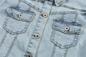 Detailed close-up of light blue washed denim jacket chest pockets and metal buttons