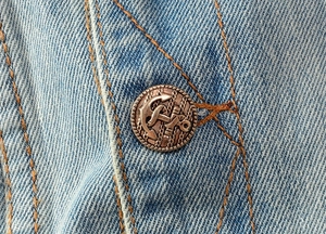 Detailansicht antiker Ankerknöpfe aus Bronze auf hellblau gewaschenem Denim-Stoff