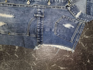 Detail der Jeansweste mit ausgefransten Taschenrändern und Metallknöpfen im Vintage-Stil