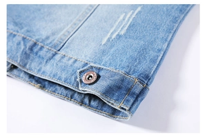 Detail of light blue denim jacket featuring bronze metal buttons and distressed hem