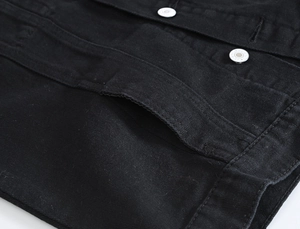 Macro detail of black denim vest featuring silver metal buttons and reinforced stitching