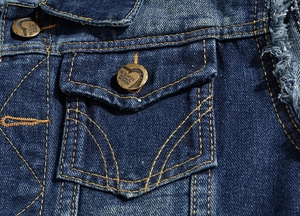 Close-up of slim-fit blue denim vest featuring distressed edges and bronze fashion buttons