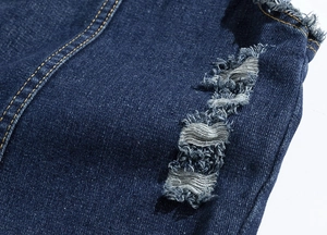 Macro shot of distressed blue denim fabric featuring ripped details and yellow stitching