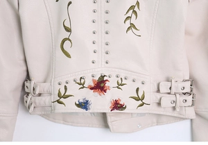 Detailed close-up of floral embroidery and silver studs on a beige faux leather jacket