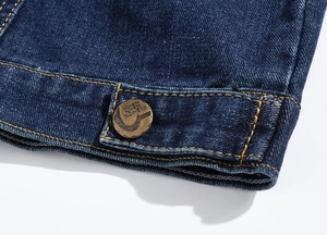 Macro detail of dark blue denim fabric with orange stitching and fashion metal button
