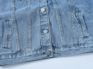 Detail view of light blue denim jacket showing metal buttons and golden stitching texture