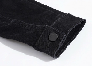 Dettaglio del polsino in denim nero con bottone in metallo opaco e incisione jeans