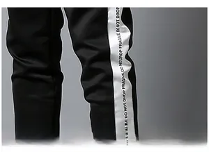 Detail of black sports trousers featuring side tape with Fragile Do Not Drop text design