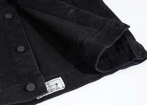 Dettaglio di una giacca di jeans nera che mostra l'etichetta cucita e i bottoni in metallo
