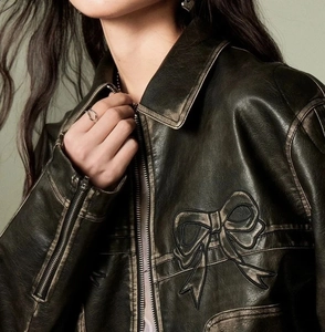 Detail of vintage brown PU leather jacket with embroidered bow and metallic zipper