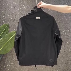 Detail of black stand-collar windbreaker featuring rectangular back logo and elastic cuffs