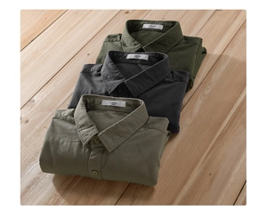 Detail of stacked cotton work shirts in olive, charcoal and khaki on a wooden background
