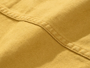Dettaglio macro del tessuto denim giallo lavato con cuciture a doppio ago robuste