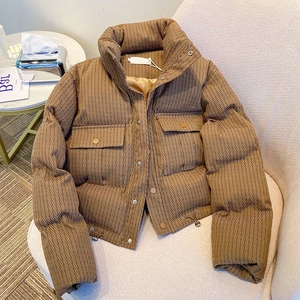 Short brown quilted puffer jacket with high collar and large pockets on a beige chair