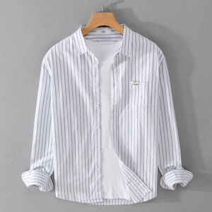Classic blue striped cotton shirt for men hanging on a wooden hanger against a grey wall