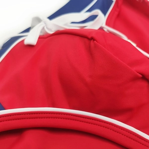 Detail of red athletic swimwear featuring blue patchwork, white piping, and adjustable drawstring