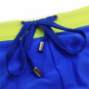 Detail of royal blue men's swim briefs featuring neon green waistband and metal-tipped drawstring