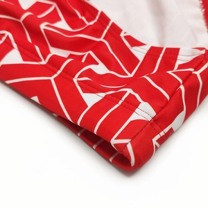 Close-up of red and white geometric patterned men's swimwear fabric with reinforced stitching
