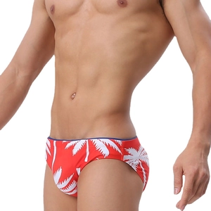 Men's red low-waisted swimming briefs with white tropical palm tree print and tight fit