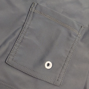 Detail view of quick-dry swim trunks featuring a metal drainage eyelet and reinforced stitching