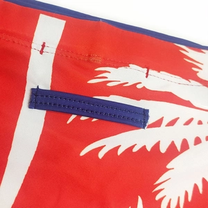 Detail of red men's swimwear with coconut tree print and reinforced blue stitching
