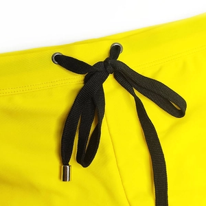 Detail of yellow swim trunks showing elastic waistband with black drawstring and metal tips