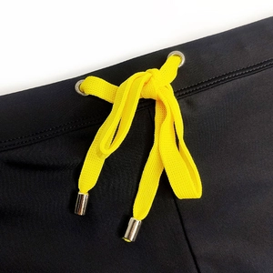 Détail d'un maillot de bain pour homme avec tissu texturé noir et cordon de serrage jaune