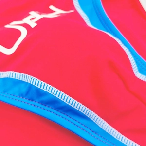 Macro detail of red men's swim briefs featuring blue elastic edging and reinforced seams