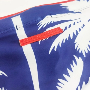 Detail of navy blue swim briefs showing white palm tree prints and red reinforced stitching