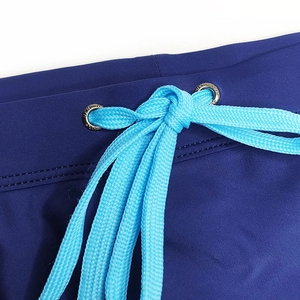 Detail view of navy swim trunks featuring bright blue braided drawstrings and silver eyelets