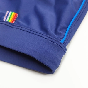 Detail of dark blue swim shorts featuring rainbow woven label and blue piping trim