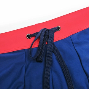 Macro view of men's swimming trunks featuring red elastic waist with navy drawstrings