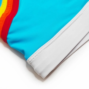 Detailed close-up of blue swim shorts featuring rainbow side stripes and elastic white cuffs
