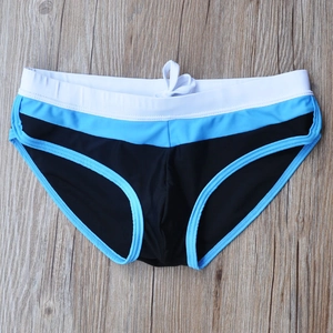 Flat lay of men's tricolor patchwork swim briefs with white drawstring on wood surface