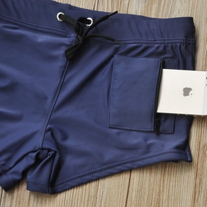 Detail of men's blue swim trunks showing vertical zipper pocket holding a smartphone