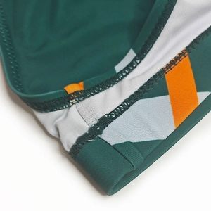Gros plan détaillé du slip de bain vert foncé avec coutures géométriques orange et blanc