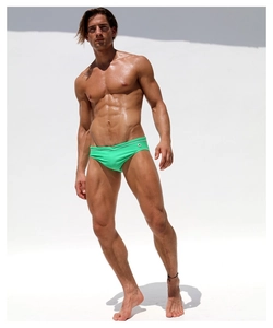 Close-up of bright green men's low-waist swim briefs with a logo detail on a fit model