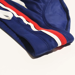 Detailed close-up of men's swim briefs showing navy fabric with red and white waist stripes