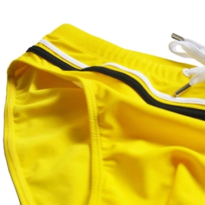 Detail of yellow swim briefs featuring a black and white striped waistband and metal-tipped drawstring