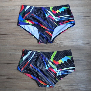 Men's swim trunks with colorful geometric print and drawstring waist on dark wood surface